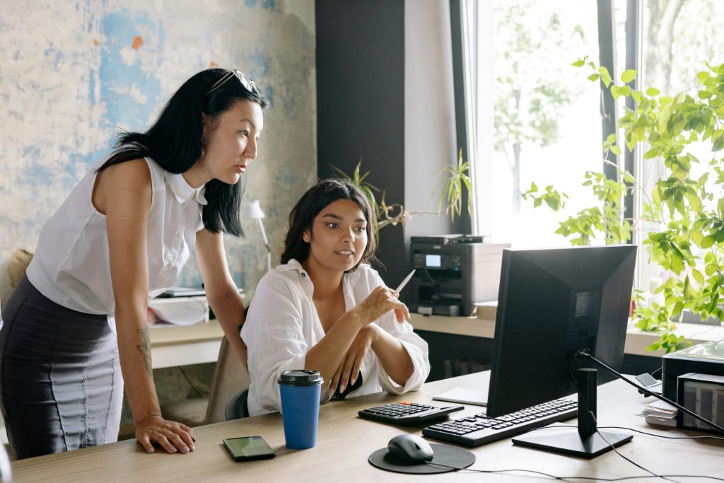 woman with long dark hair looking over shoulder of seated female colleague